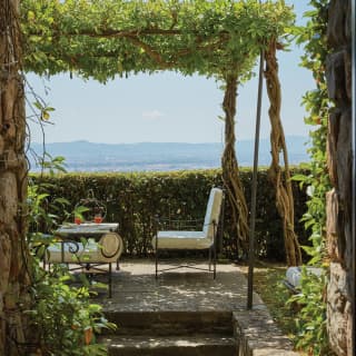 Cushioned garden chairs and table enjoy views of the Arno Valley under the dappled shade of a leafy arbour