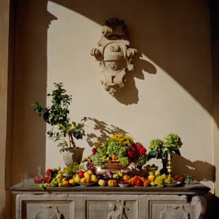 A stone altar-like table is adorned with a rainbow of produce including lemons, limes, pumpkins, grapes, cherries and flowers