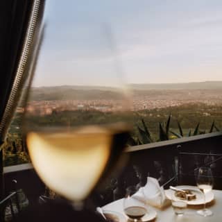 A close up image of a glass of white wine fades into a long view of Florence, its white walls and red roofs surrounded by green
