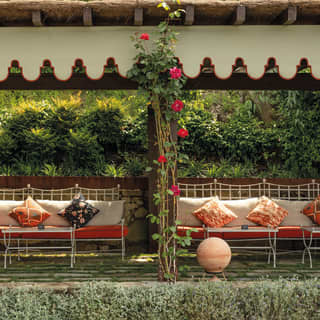A row of garden benches, adorned with brightly coloured cushions, sits in the shade of a pergola on a verdant hill terrace