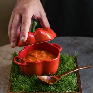 Close-up of a red pepper risotto served in a red pepper-shaped bowl beside a wooden spoon