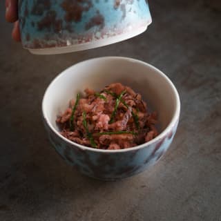 Close-up of a blue marble egg-shaped bowl containing pink crisped squid and samphire