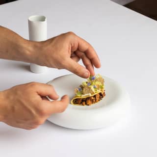 Close-up of hands placing delicate edible flowers on a mushroom ravioli dish