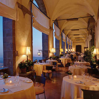 An elegant restaurant extends the length of a vaulted loggia, its arches revealing stunning views of Florence as night descends