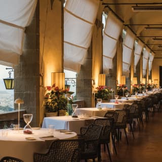 A row of linen-topped circular tables on a lamplit open-air restaurant terrace
