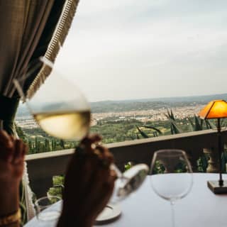 In soft-focus foreground, a guest of La Loggia raises a glass of white wine at a table overlooking Florence's pretty sprawl.