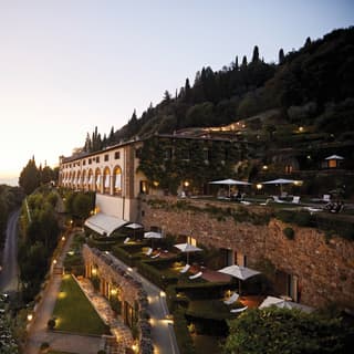 Hilltop monastery with tiered lamplit gardens and views of sunset over Florence