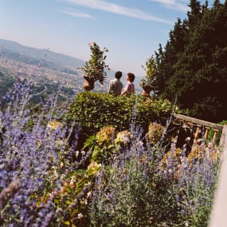 Angled image of two guests standing on the stone terrace in a garden bursting with lavender and foliage overlooking Florence.