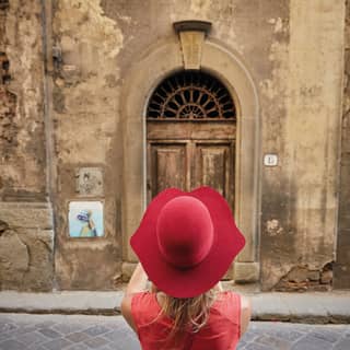 Lady in a red wide-brimmed hat taking a photograph of an old Florentine street