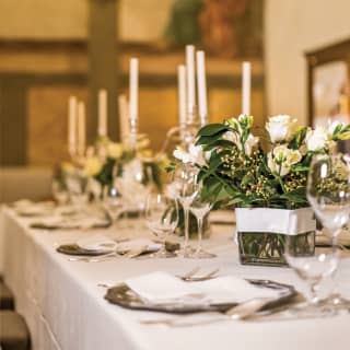 A wedding table is set with white candles and vases of white roses and freesias. Behind the arches is a painted wall fresco