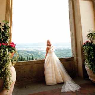 Bride in a wedding dress leaning against a stone arch with views of the hills of Fiesole