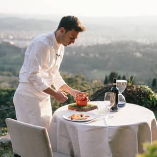 Executive chef, Alessandro Cozzolino, prepares a dish at a table on the garden terrace overlooking views of Florence