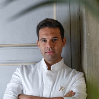 Executive chef, Alessandro Cozzolino, leans against a stone wall in his chef's whites, his arms folded and his sleeves rolled up