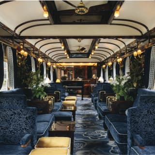 View of the opulent bar car with carpet and plush seating in rich blue, with warm gold in the lighting and velvet stools.