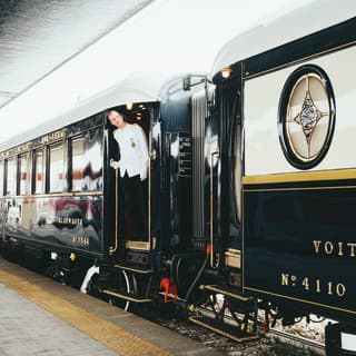 Train steward in a white formal jacket gazing down the exterior of a luxury train carriage