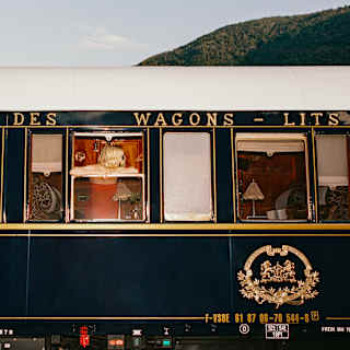 A blonde woman leans on an open carriage window, head turned to the side, in an exterior view of the black and white train.