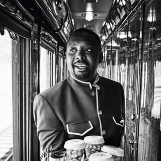 Fotografía en blanco y negro de un camarero de tren en un corredor angosto con paneles de madera