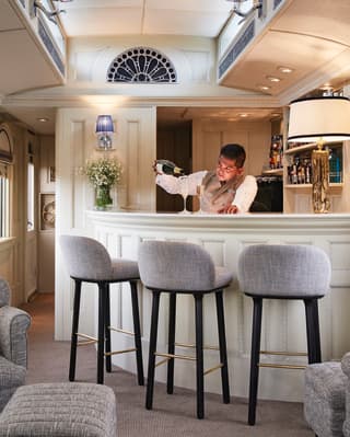 Barman in a train bar car pouring champagne into a flute glass