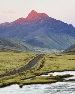 Andean mountain tipped pink by the sun with a train track running from the base