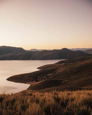 A sunset view of Lake Saracocha with its tranquil waters and soft contours bathed in golden hues.