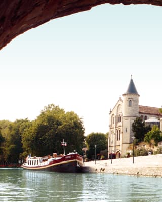 River barge moored beside a medieval French village viewed through a stone arch