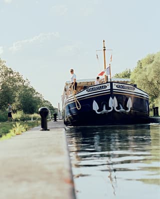 Water-level view of the Amaryllis on a narrow section of the Canal du Centre, about to be moored by a man holding a rope.