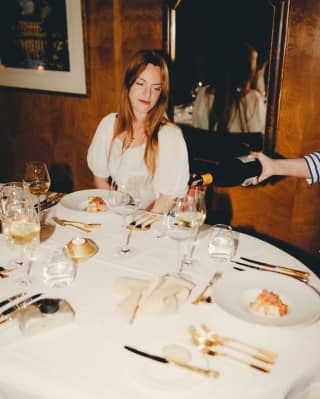 At a dining table, a female guest watches as white wine is decanted into her glass, before tasting her elegant starter dish.