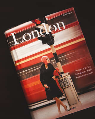 An antique silver writing set with double inkwell and two pens sits beside a hardback Taschen art book of London images