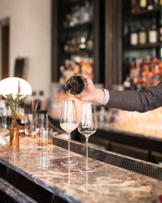 Barman pouring champagne into two champagne flutes on a marble bar