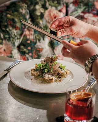 Close-up of a hand grating a truffle over a mushroom dish