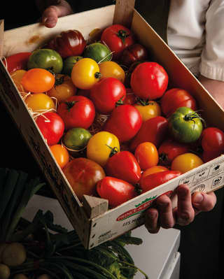Chef holding a wooden box full of colourful tomatoes 