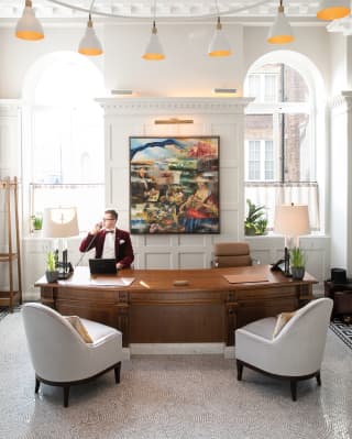 Concierge at a curved wooden desk with two warm grey armchairs in front