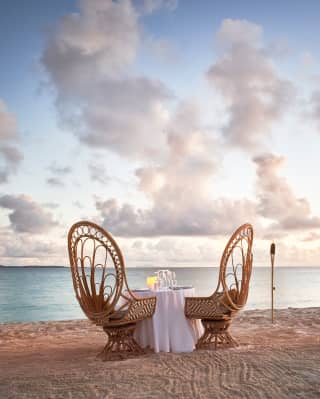 Two curved wooden chairs at a table on an Anguillan beach at sunset