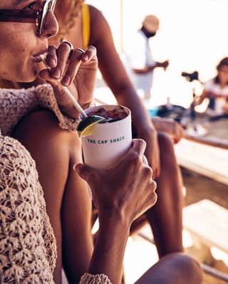 Lady sipping a cocktail through a straw from a cup emblazoned with the words: 'The Cap Shack'