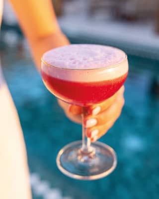 Close-up of a hand holding a cosmopolitan cocktail topped with pink foam in a cockatil glass