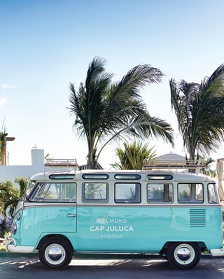 Light-blue VW camper van against sunny blue-skies and palm trees