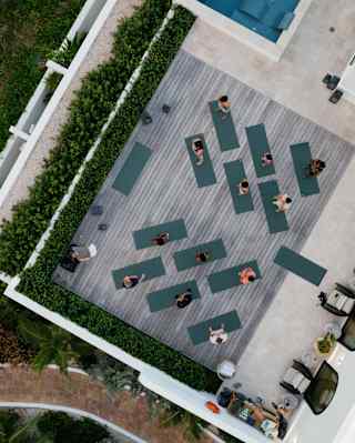 Bird's-eye view of a yoga class with twelve participants on the spa deck by an infinity pool in the lush resort surrounds.