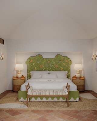 View of the airy Divina Suite bedroom with side tables and lamps either side of a large bed with green embroidered headboard.