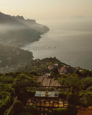 High view from Caruso over the Krug Table terrace and foliage-filled hills, down to the town rooftops and boat-dotted ocean.