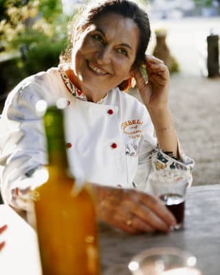 Italian chef, Giovanna Voria, smiles as she drinks an aperitif. Her chef's whites are branded Corbella, decorated with red buttons