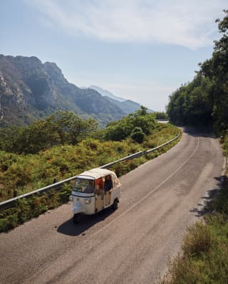 Traditional Ape Calessino car motoring along a hilltop road surrounded by lush foliage