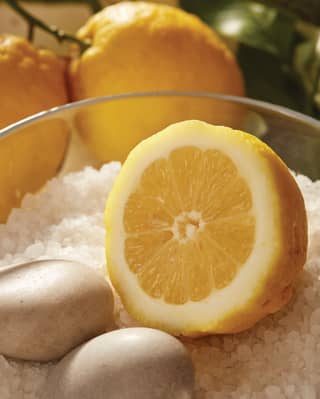 A fresh cut lemon half sits in a glass bowl of sea salt crystals and marble eggs