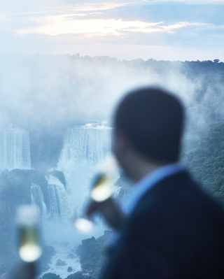 A man and woman with champagne glasses look out over the spectacular misty cascades of the Iguassu Falls