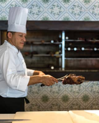 A hotel chef prepares cooked skewered meat ‘gaucho’ style in front of a barbecue oven at Ipe Grill