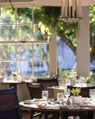 Circular table with rattan chairs and wine glasses reflecting the sunlight