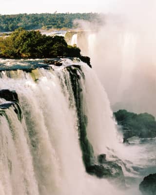 Dramatic shot of Iguassu Falls as white water thunders over the rocky brink and clouds of mist and spray dance in the air.