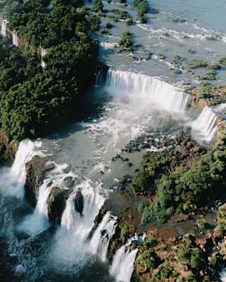 Aerial view of the dramatic Iguassu Falls, tumbling over two levels of rocky ledges, bordered by vegetation.