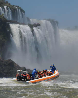 An orange speed raft with guests on board approaching the Iguassu Falls