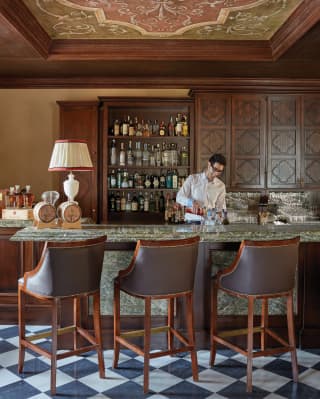 Barman mixing a cocktail at a green marble counter fronted by leather barstools