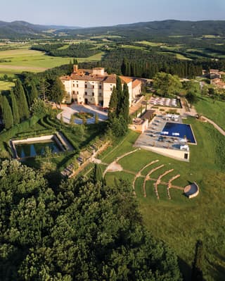 Aerial view of a sprawling castle with an outdoor pool and open-air amphitheatre